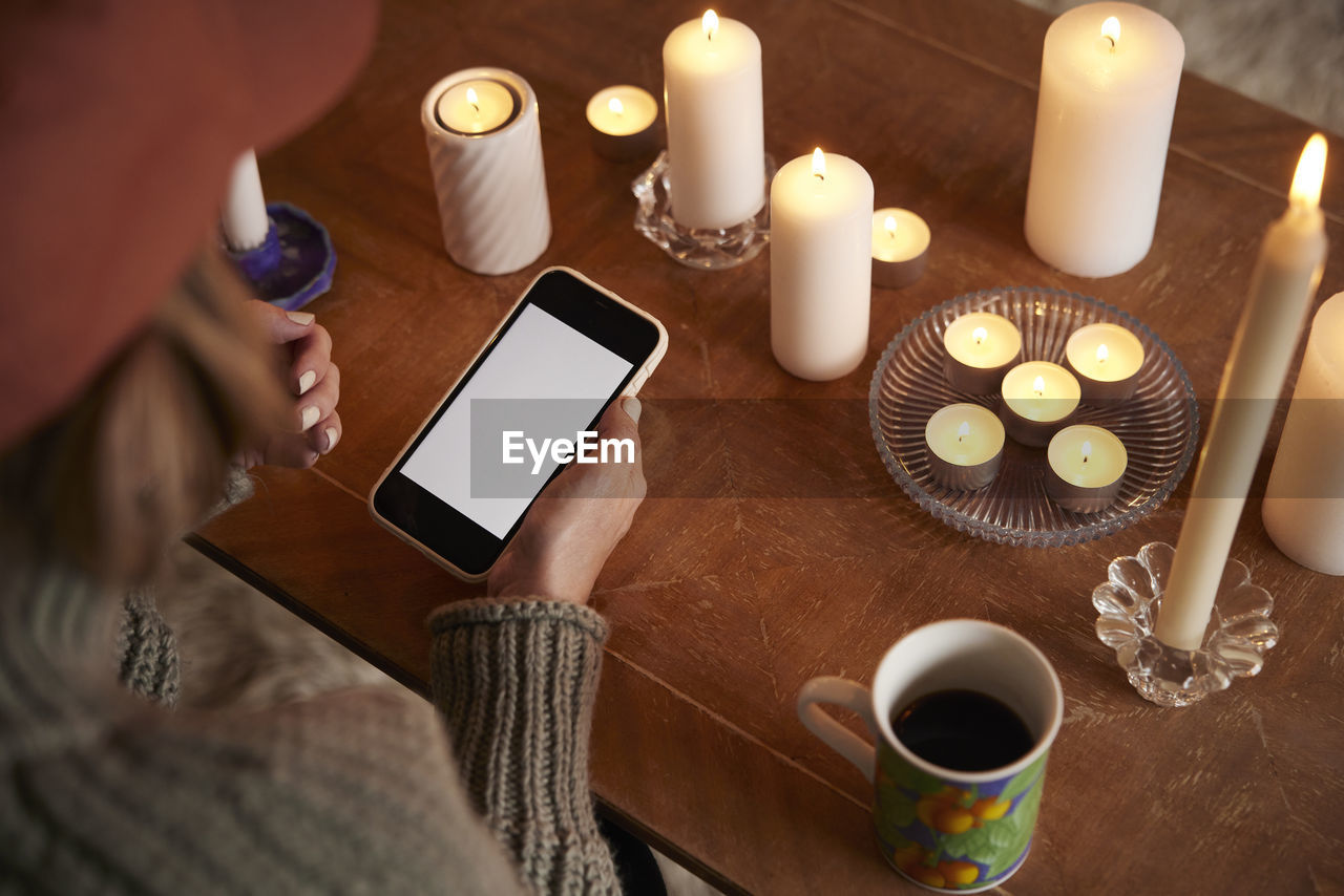 Woman using phone next to lit candles