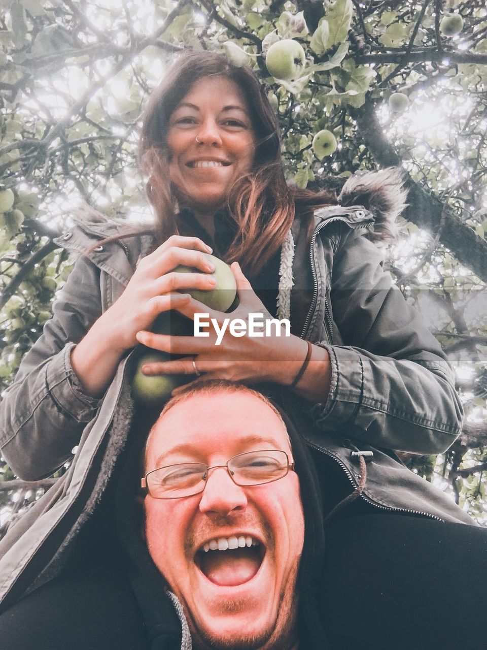 Portrait of smiling woman holding fruits over man against tree