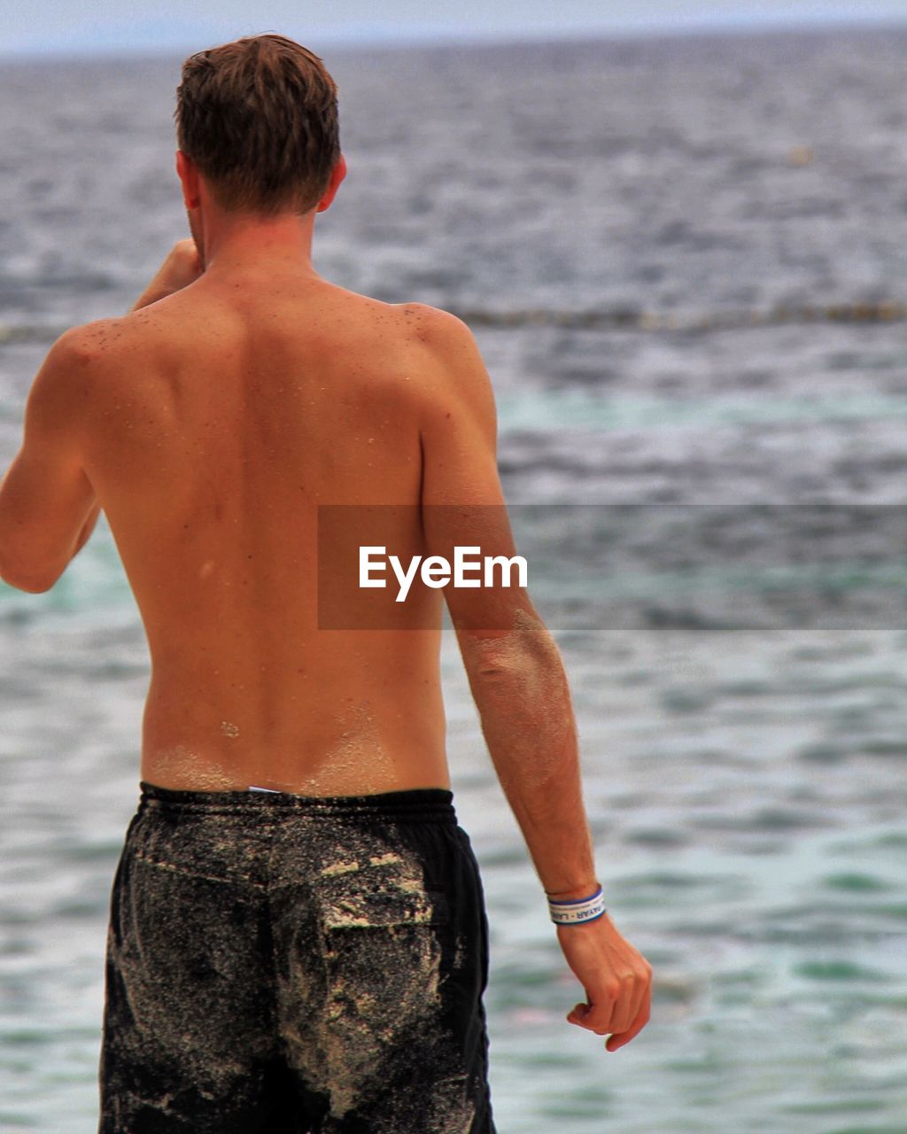 Rear view of shirtless man standing at beach