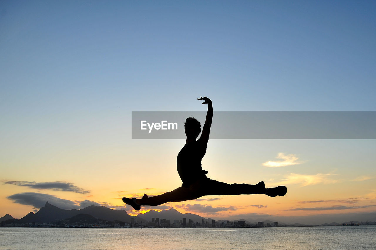 Silhouette man jumping above sea against sky during sunset