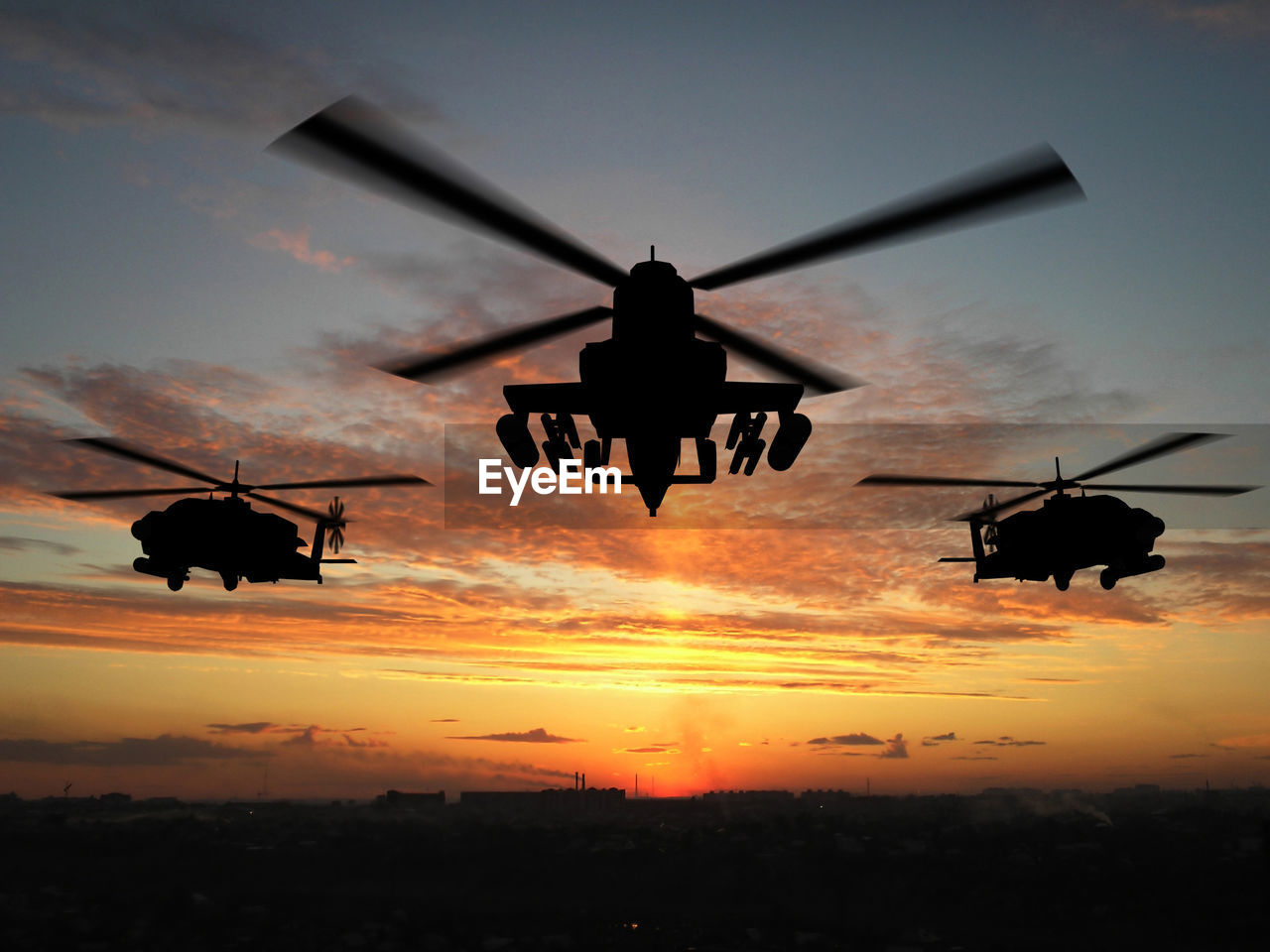 Military helicopters flying over cityscape against sky during sunset