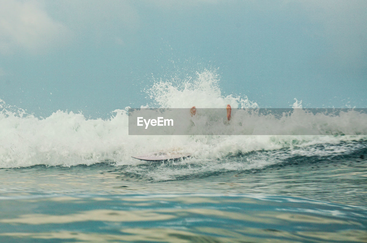 Low section of person surfing on sea against sky