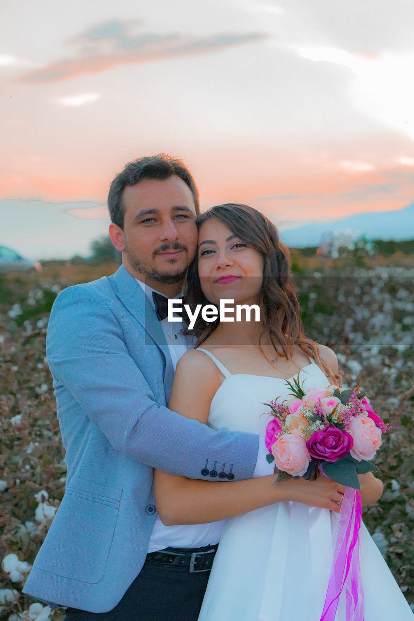 Portrait of smiling bride and groom with bouquet romancing on field