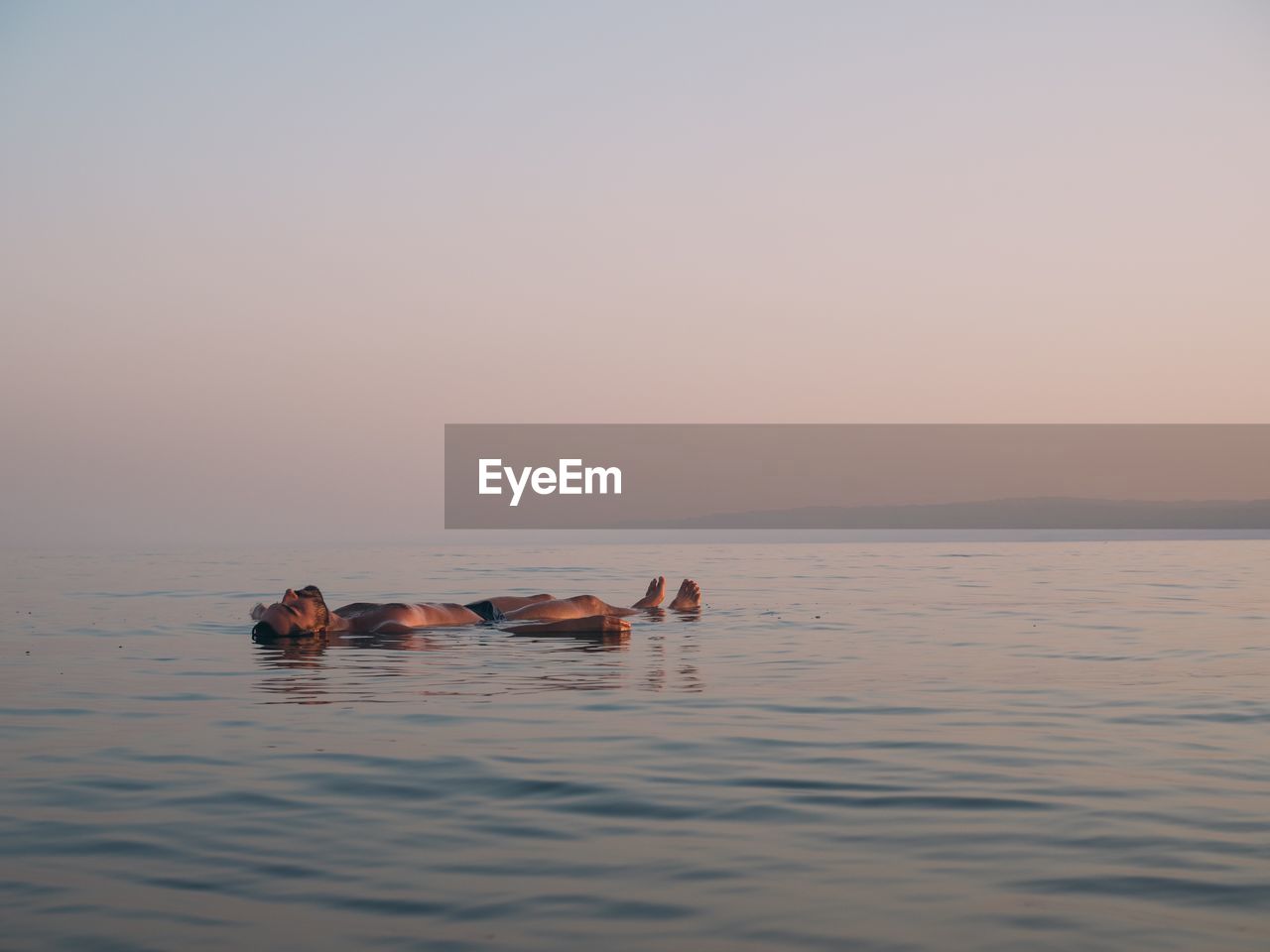 Man swimming in sea against sky during sunset