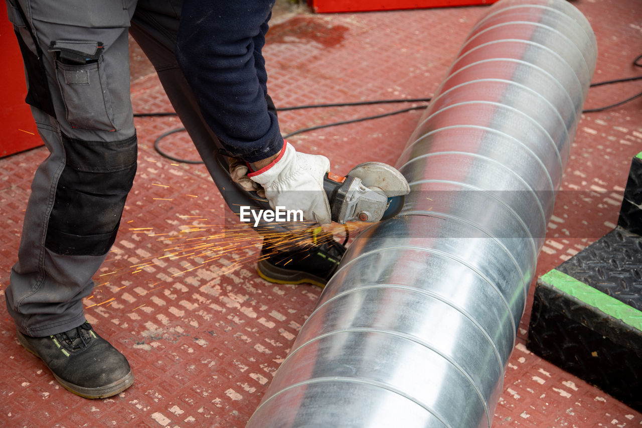 Low section of manual worker cutting metal pipe with grinder