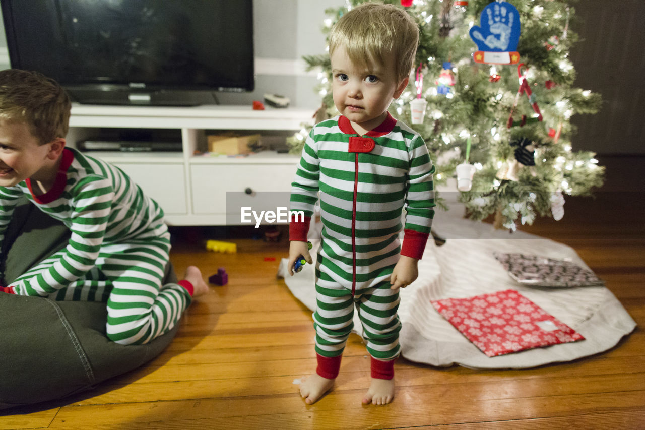 Toddler boy standing in front of christmas tree in green striped pjs