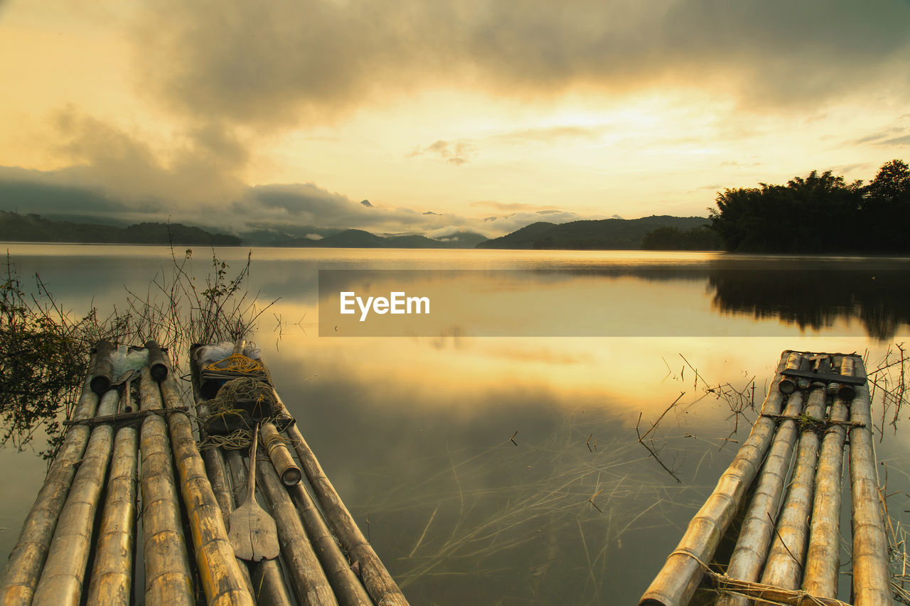 WOODEN POSTS IN LAKE AGAINST SKY AT SUNSET