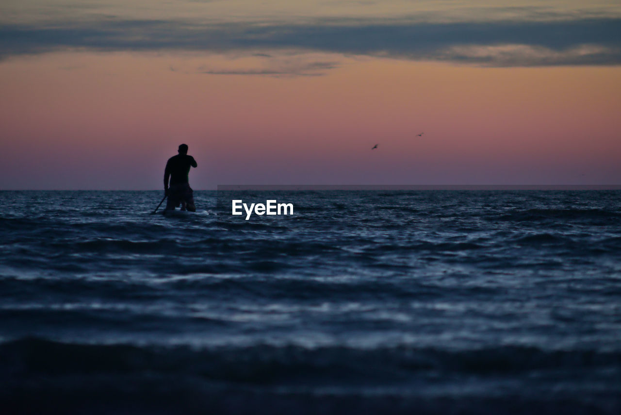 Silhouette man walking in sea against sky during sunset