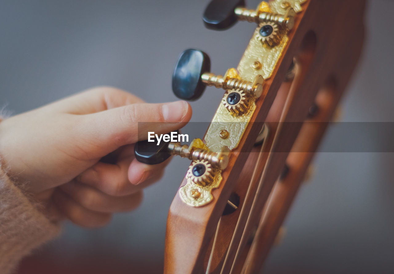 The girl twists the guitar peg while tuning the strings.