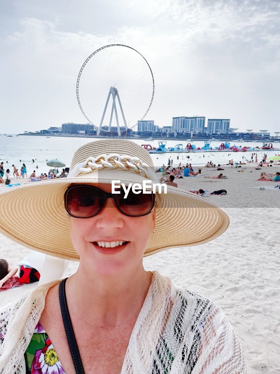 Portrait of smiling mature woman wearing sunglasses and hat at beach against sky