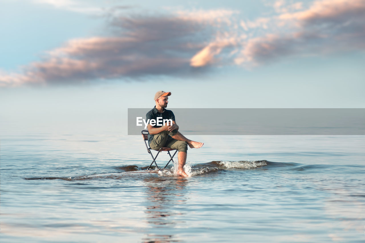 Man sitting on chair at beach against sky