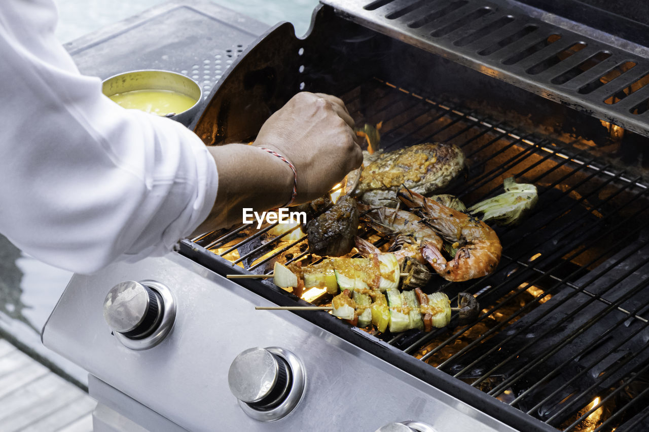 cropped hand of man preparing food on barbecue grill