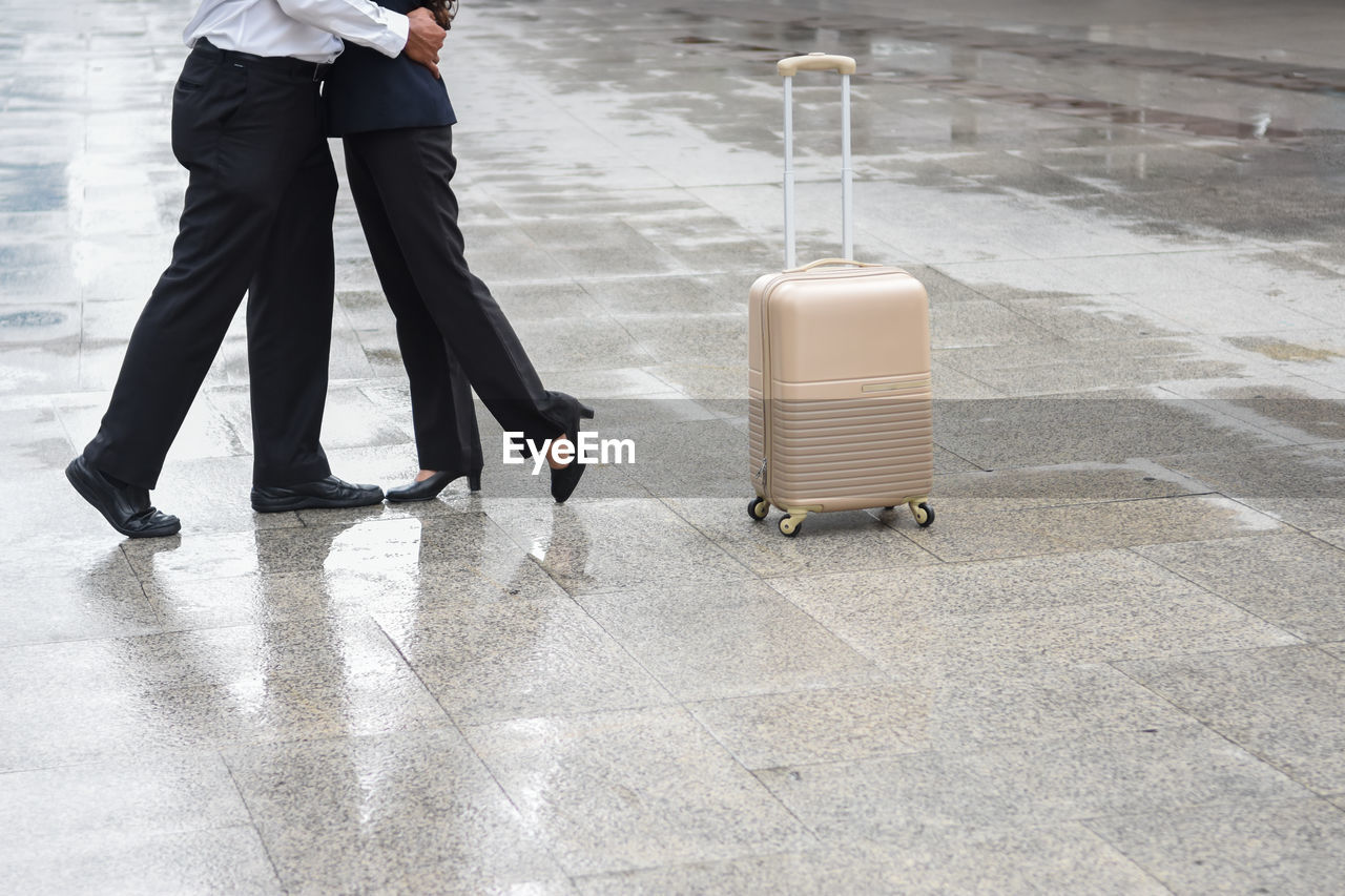 Low section of couple standing by luggage on footpath