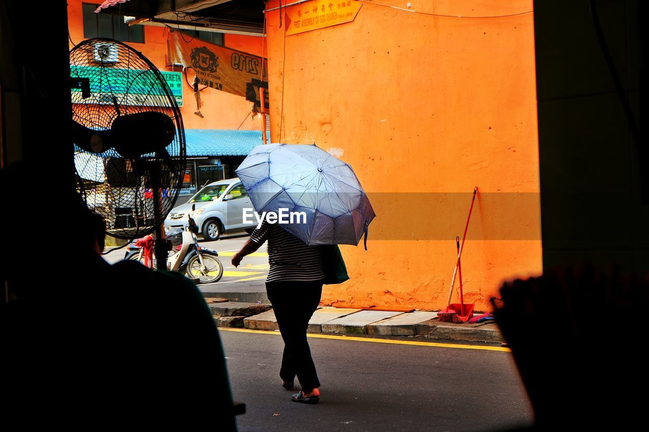 Woman with umbrella walking by building on street in city