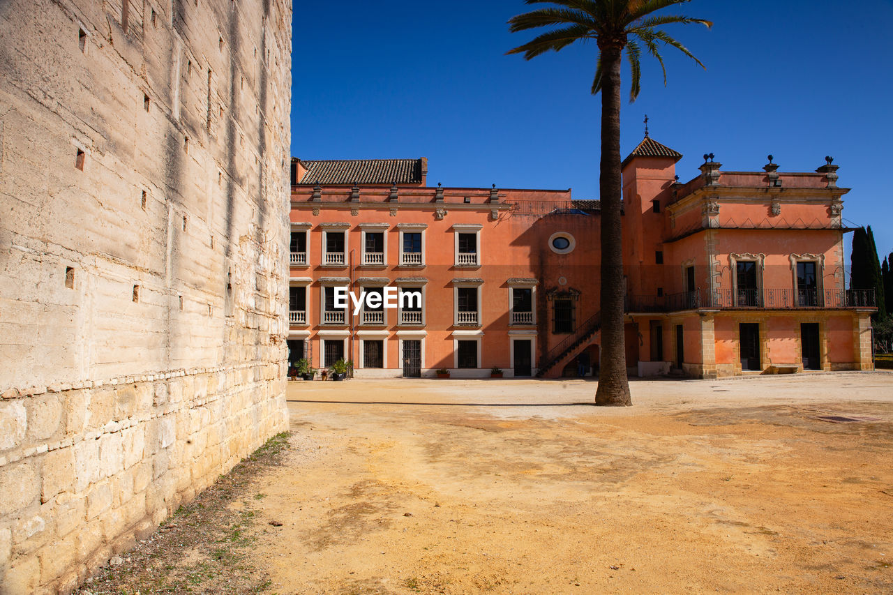 architecture, built structure, building exterior, palm tree, history, the past, travel destinations, ancient history, sky, building, nature, tropical climate, city, tree, clear sky, wall, town, travel, no people, urban area, blue, plant, outdoors, mansion, sunny, estate, tourism, street, brick