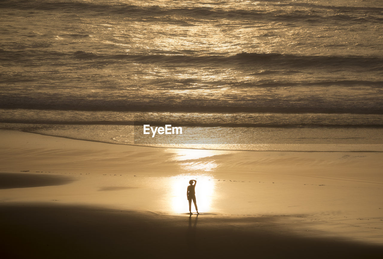 SILHOUETTE MAN STANDING ON BEACH AGAINST SUNSET SKY