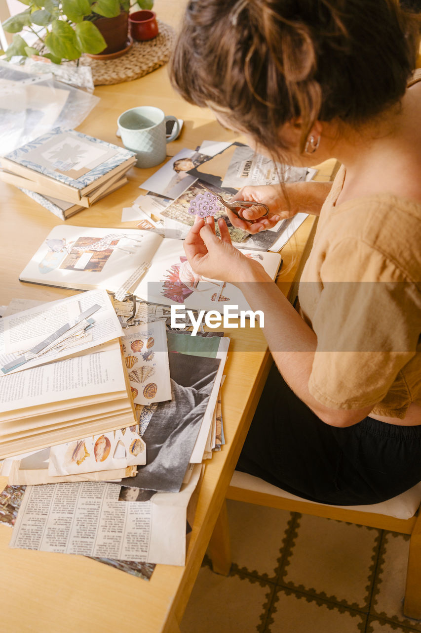 Graphic designer cutting paper clipping sitting at desk in home