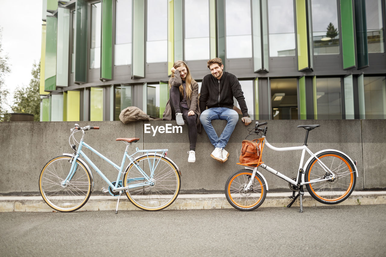 Happy couple with bicycles sitting on a wall