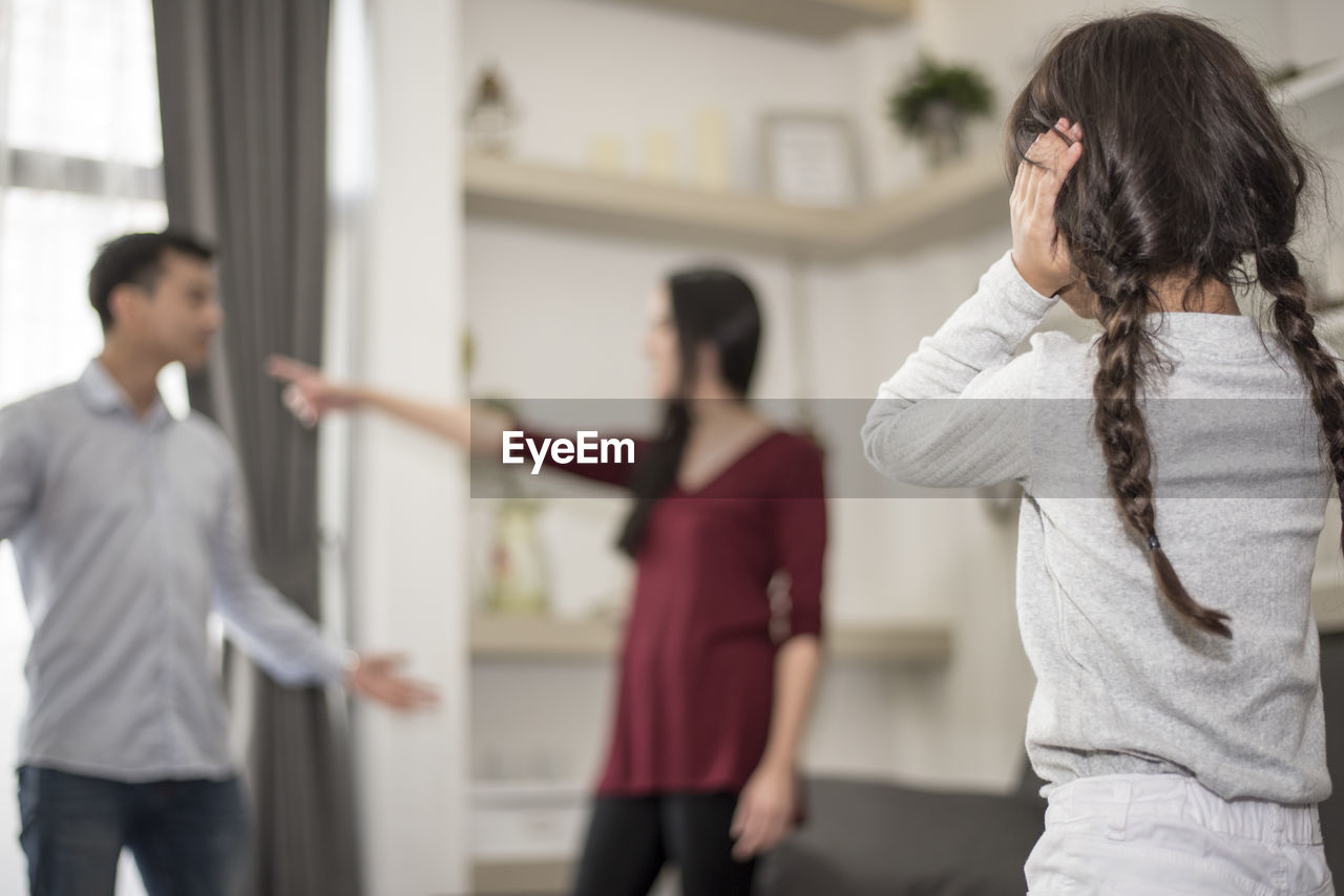 Girl covering ears while parents arguing at home