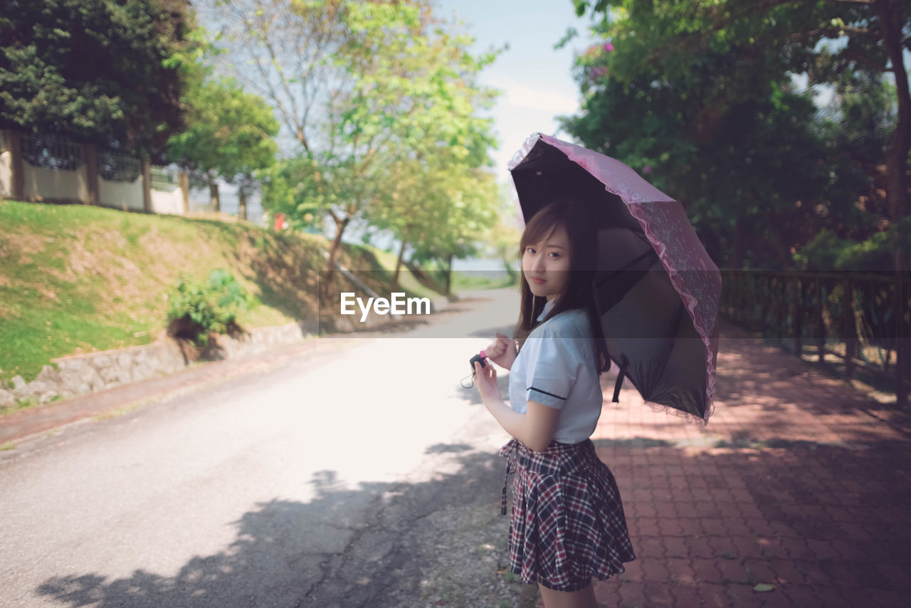 Portrait of woman with umbrella standing on road against trees