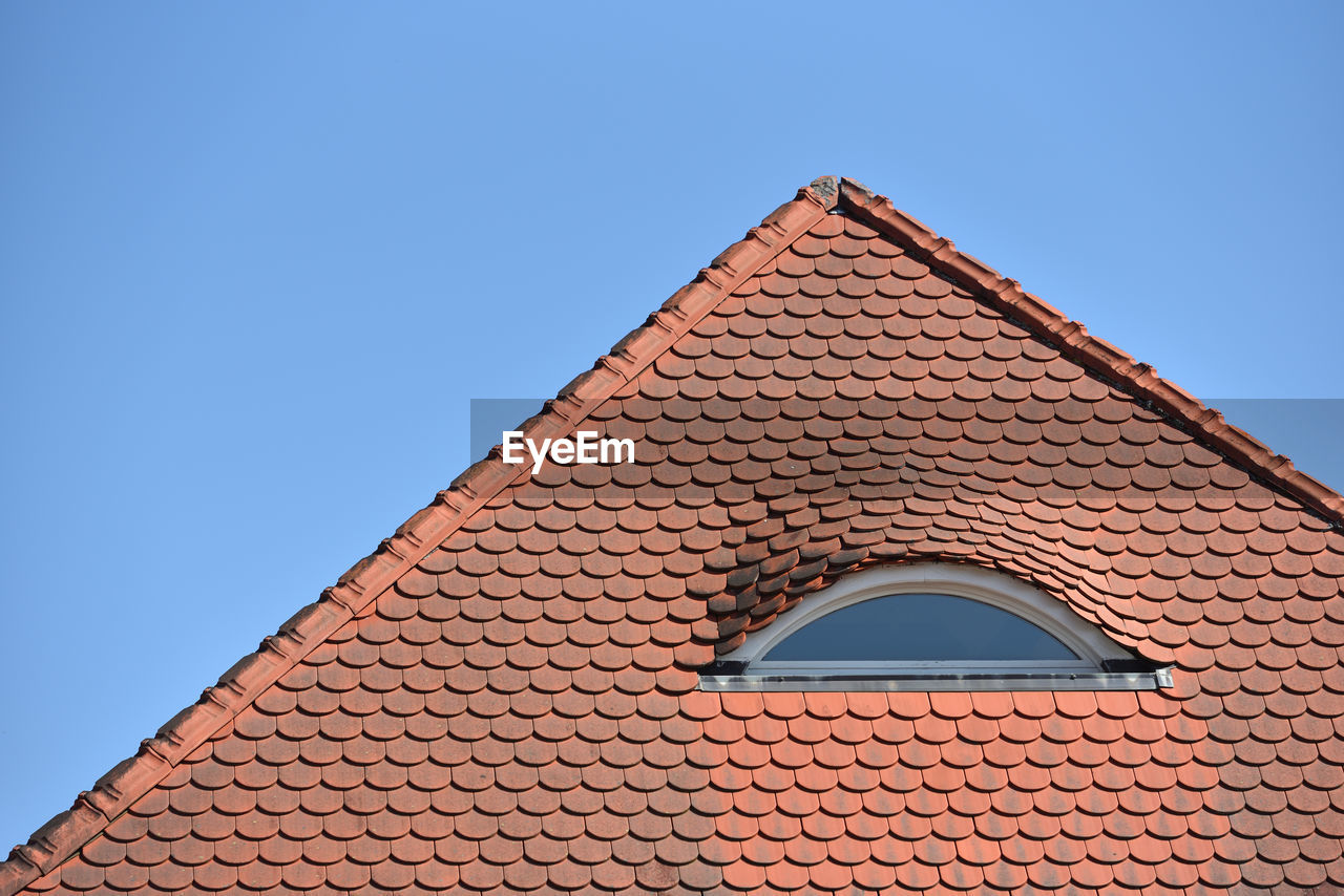 Low angle view of building tiles roof against clear blue sky