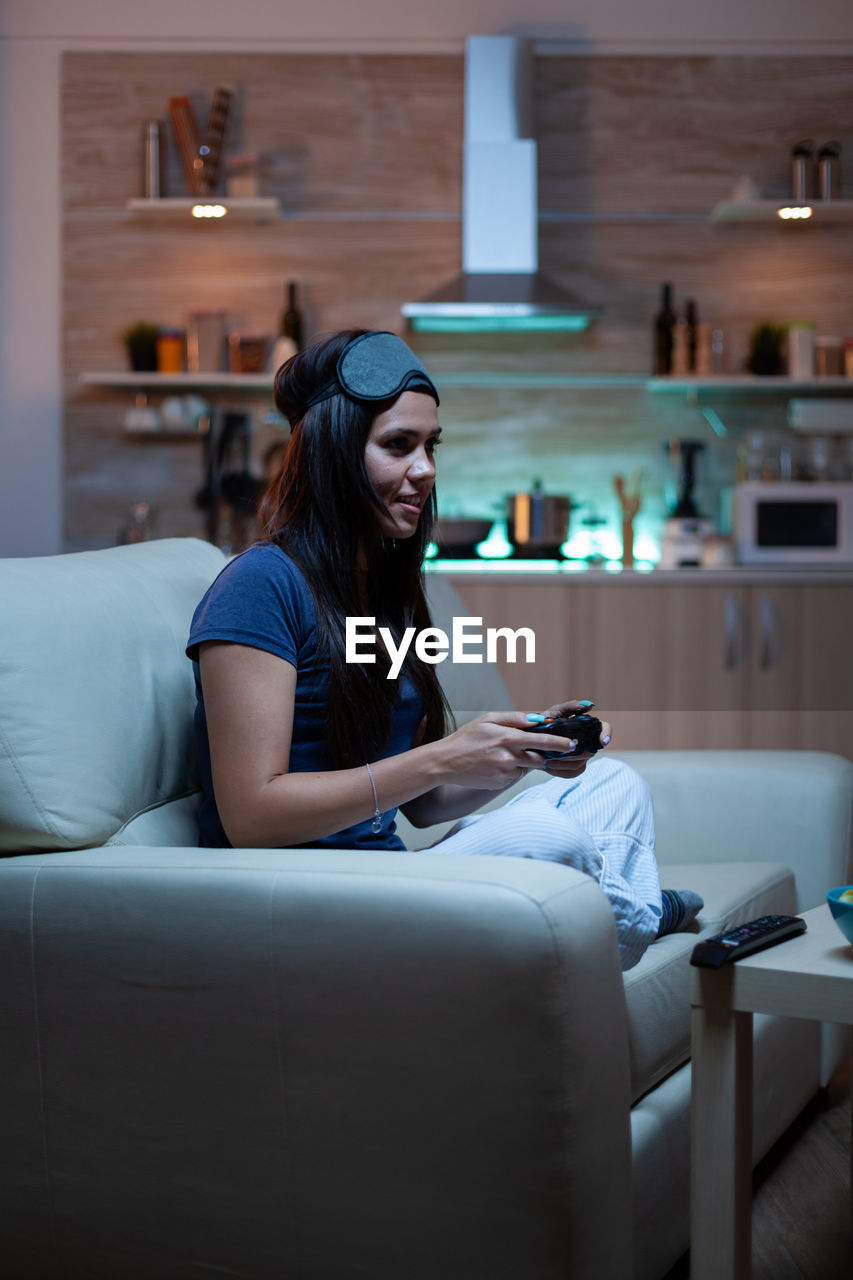 young woman using mobile phone while sitting on sofa at home