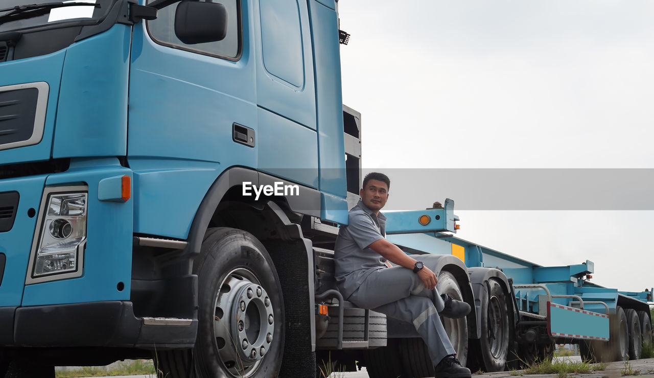 Side view of man looking away while sitting on truck against clear sky