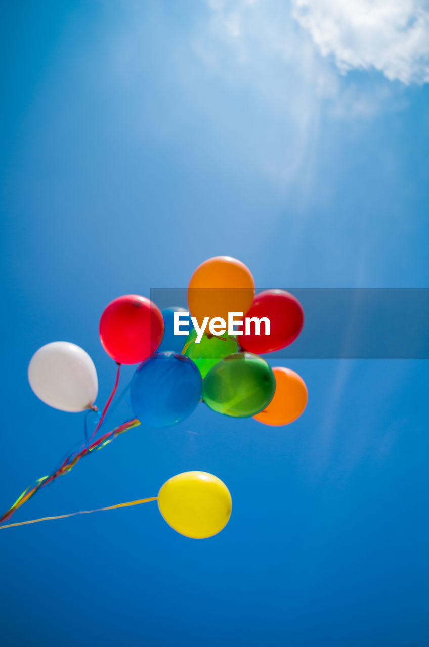 Low angle view of colorful helium balloons against sky