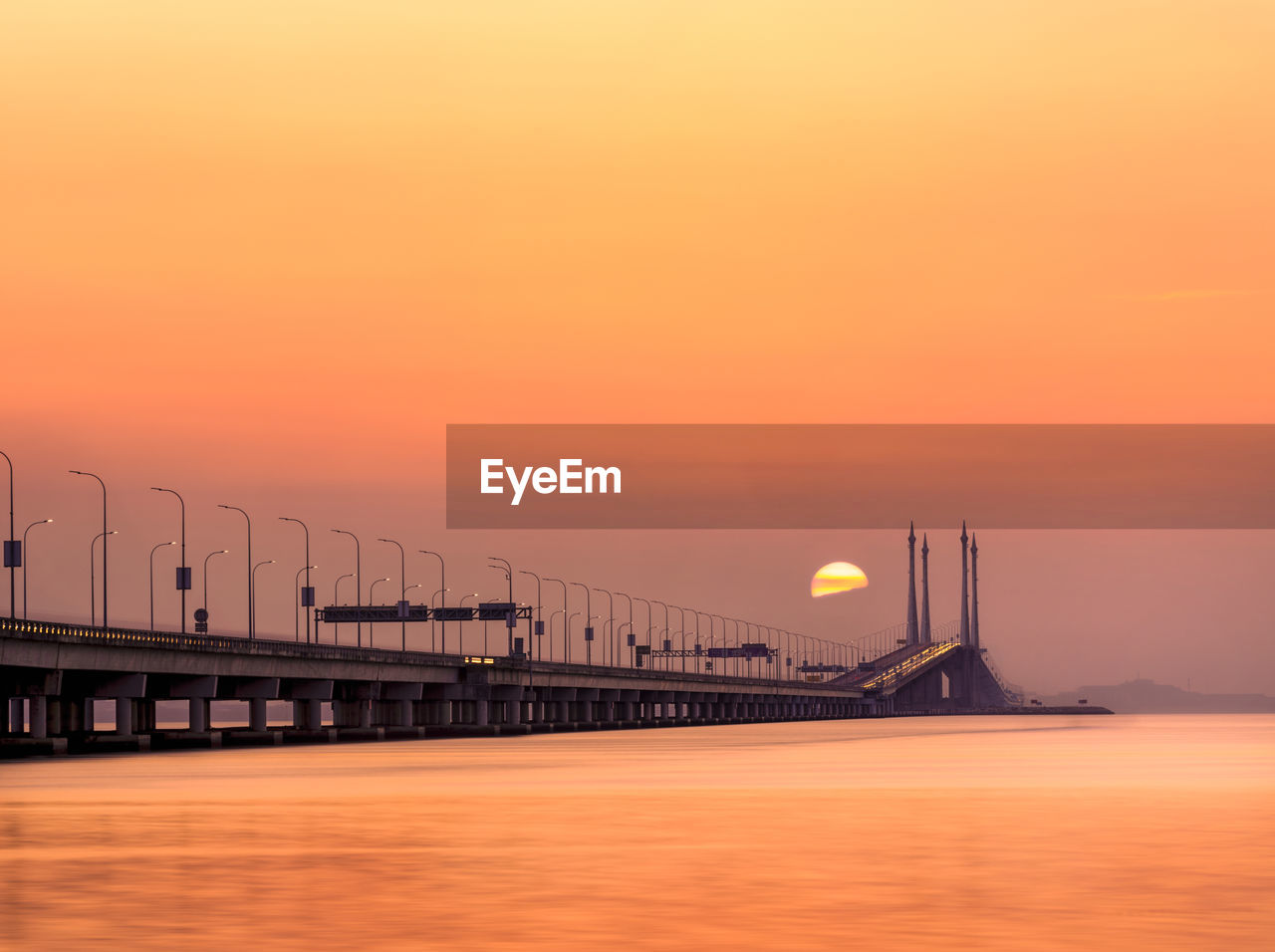 SCENIC VIEW OF BRIDGE OVER SEA AGAINST ORANGE SKY