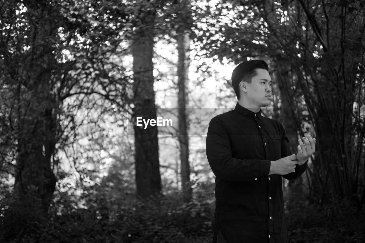 Thoughtful man in traditional clothing looking away while standing against trees