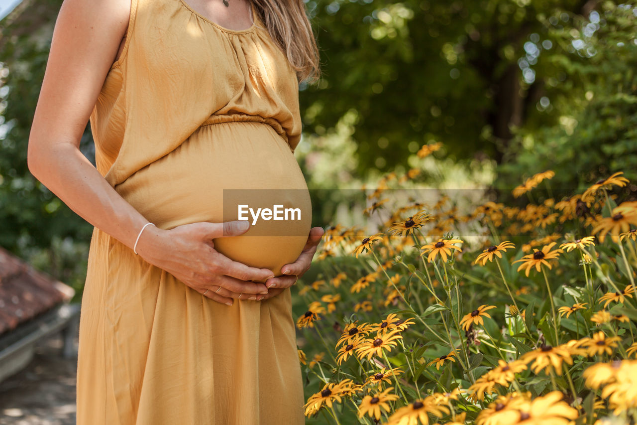 Midsection of pregnant woman holding stomach while standing outdoors