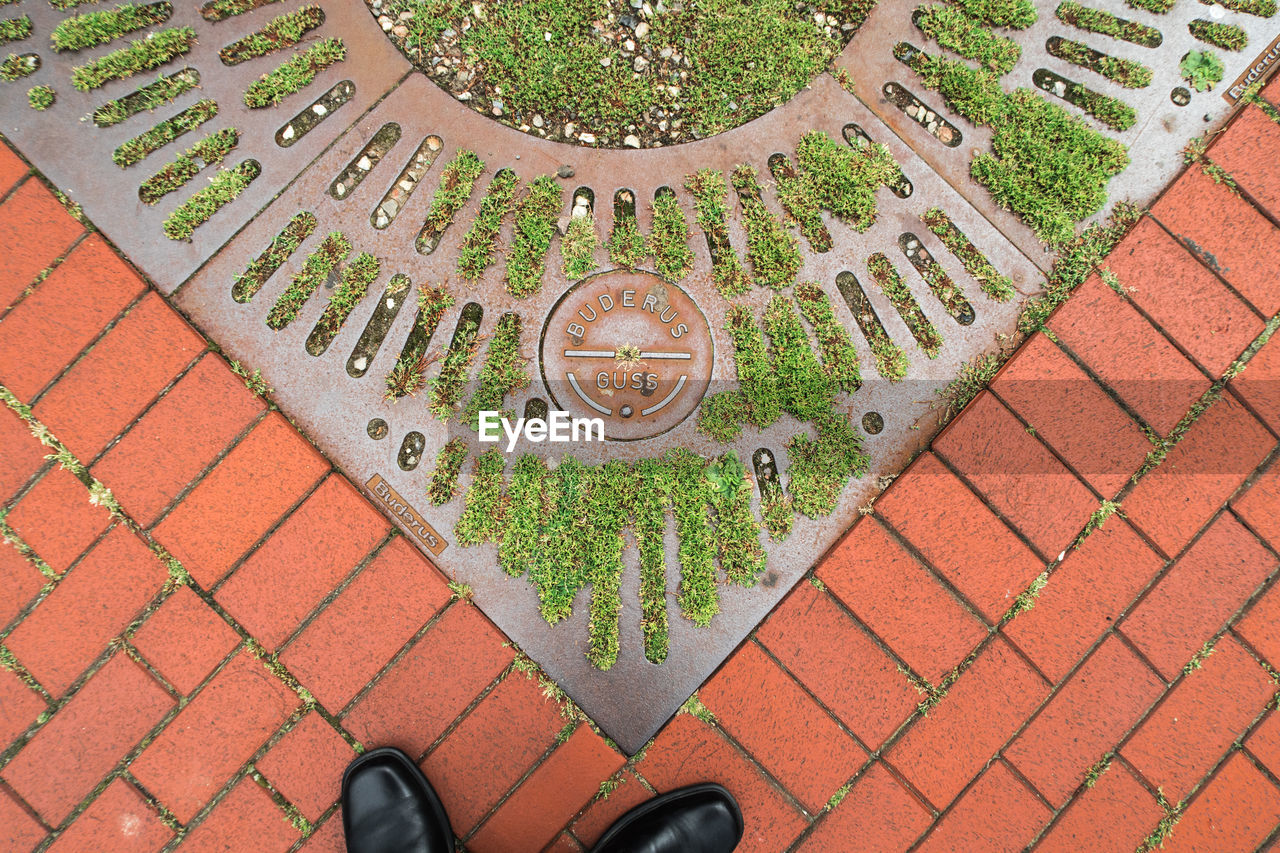 CLOSE-UP HIGH ANGLE VIEW OF MANHOLE ON WET COBBLESTONE