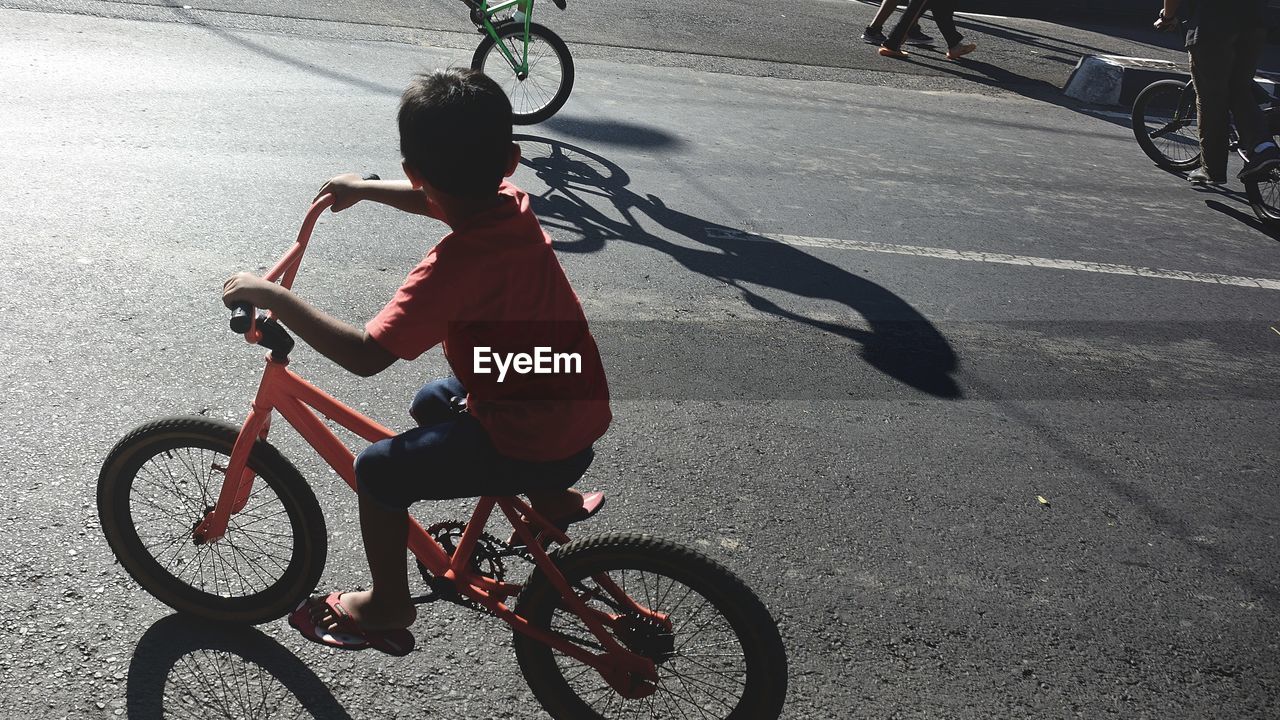 Boy riding bicycle on road during sunny day