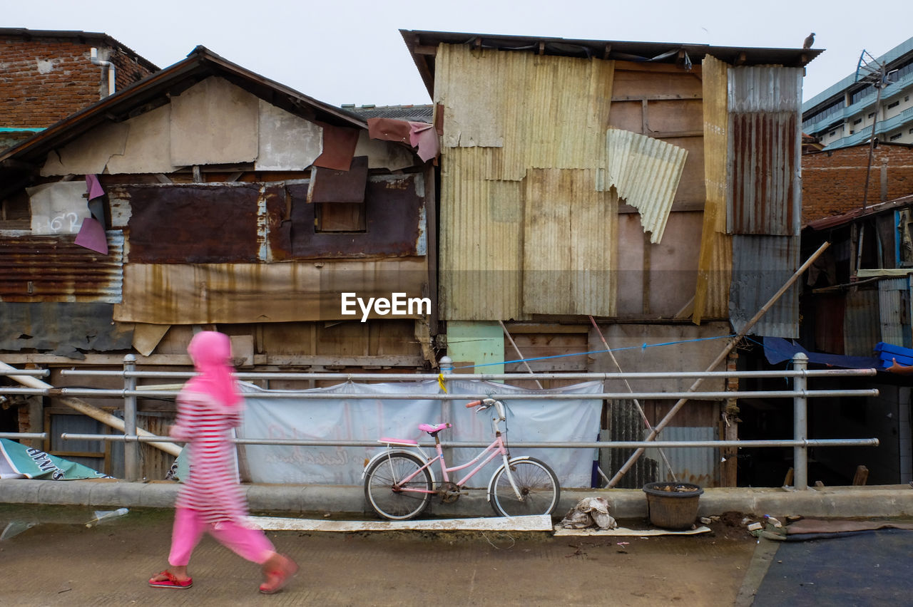 SIDE VIEW OF GIRL HOLDING UMBRELLA WALKING IN FRONT OF BUILDINGS