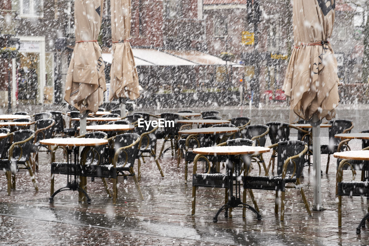 Empty chairs and tables by a restaurant, outdoors in the snow