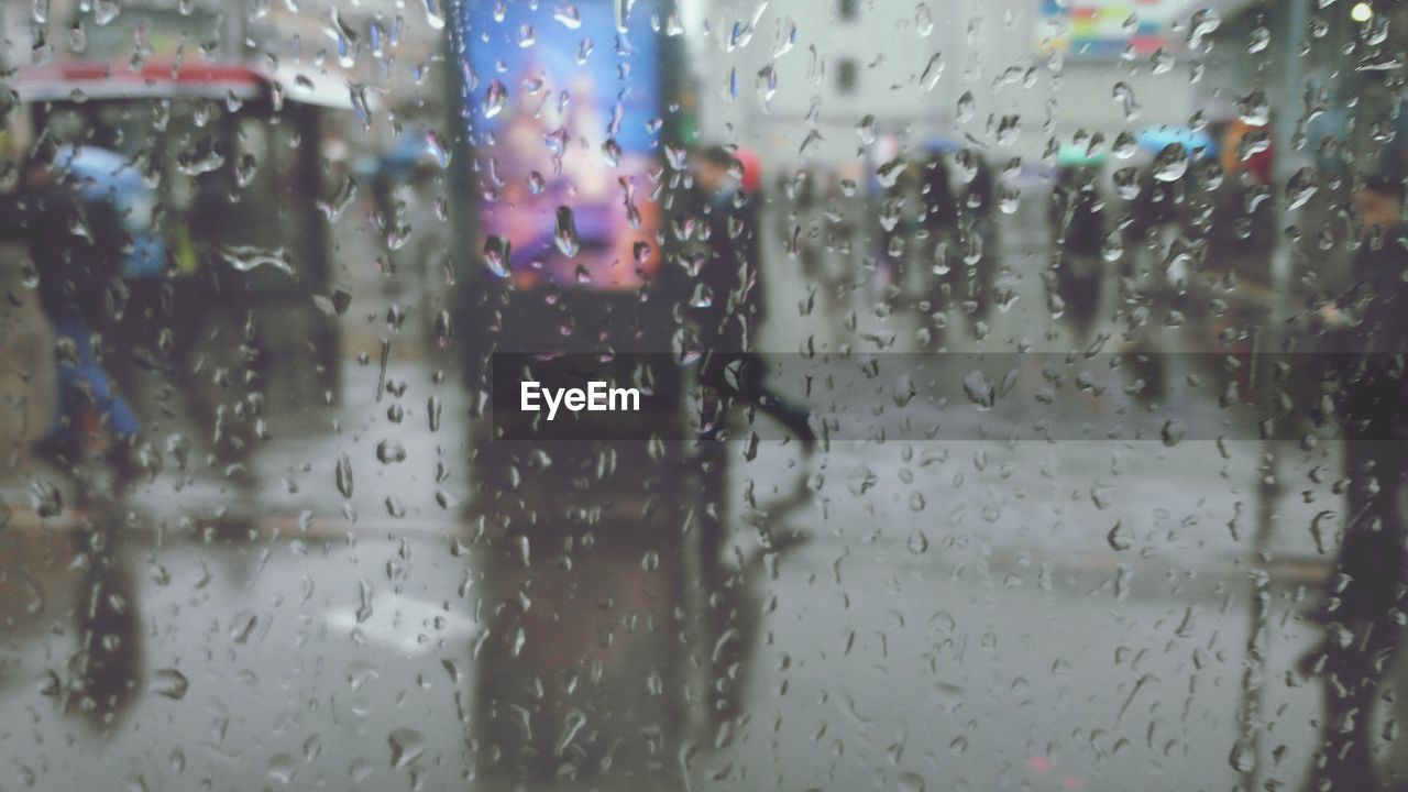 People walking on street seen through wet car window during monsoon