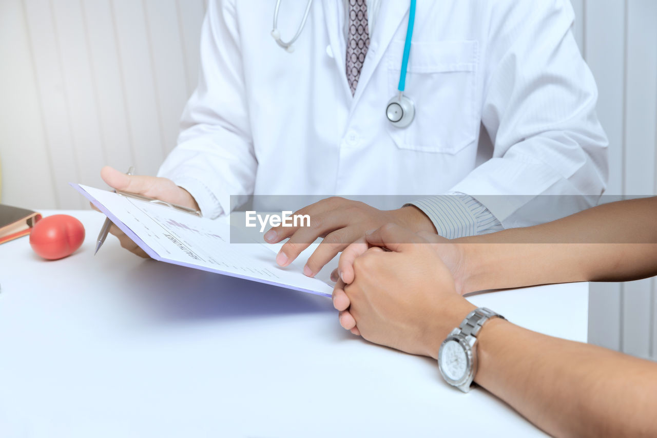 Midsection of doctor explaining medical records to patient