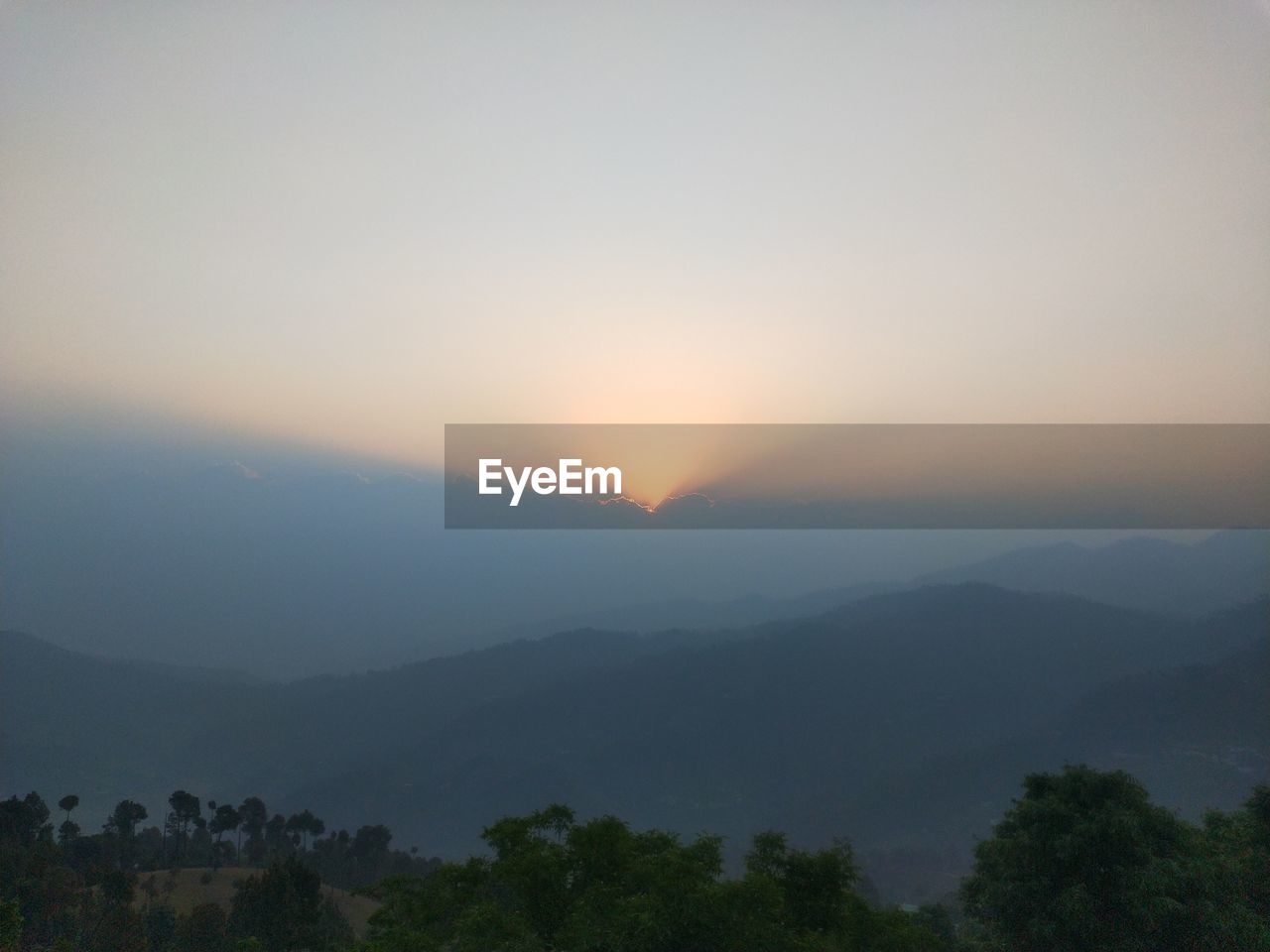 SCENIC VIEW OF TREES AND MOUNTAINS AGAINST SKY AT SUNSET