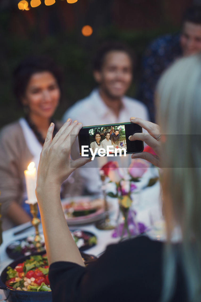 Woman photographing friends through smart phone at garden party
