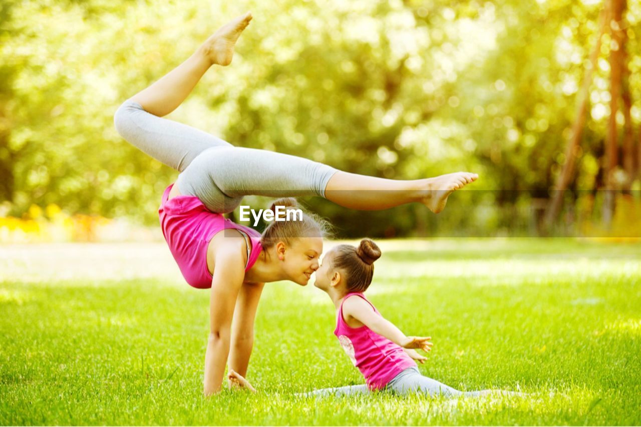 Full length of mother and daughter practicing yoga on grass