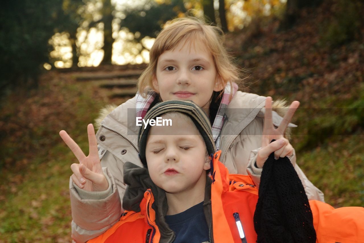 Siblings gesturing peace sign at park during sunset