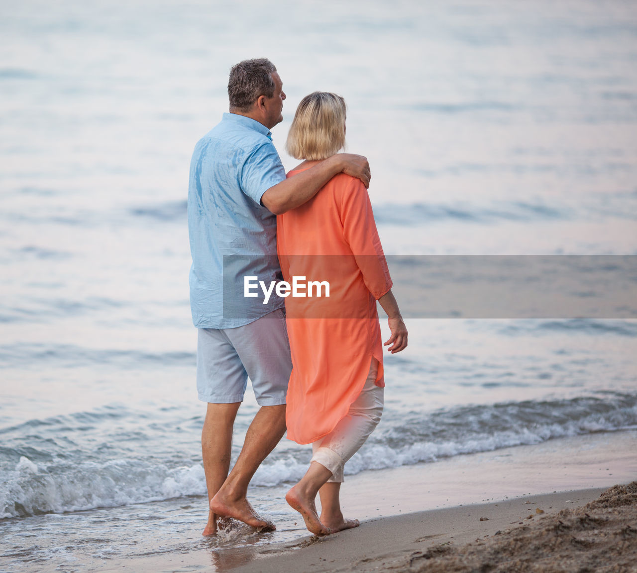 Side view of couple walking at beach during sunset