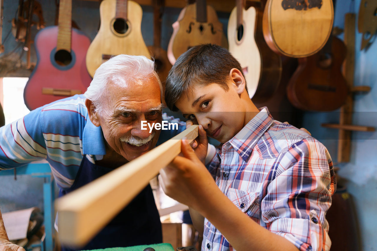 Senior man looking at boy holding wood in workshop