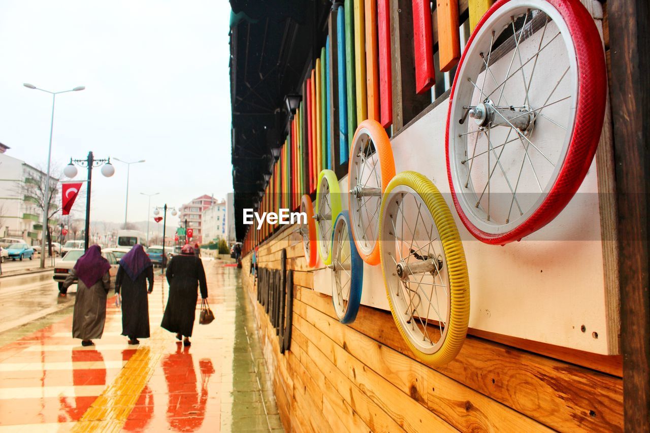 Colorful wheels on wall with people walking on sidewalk in city