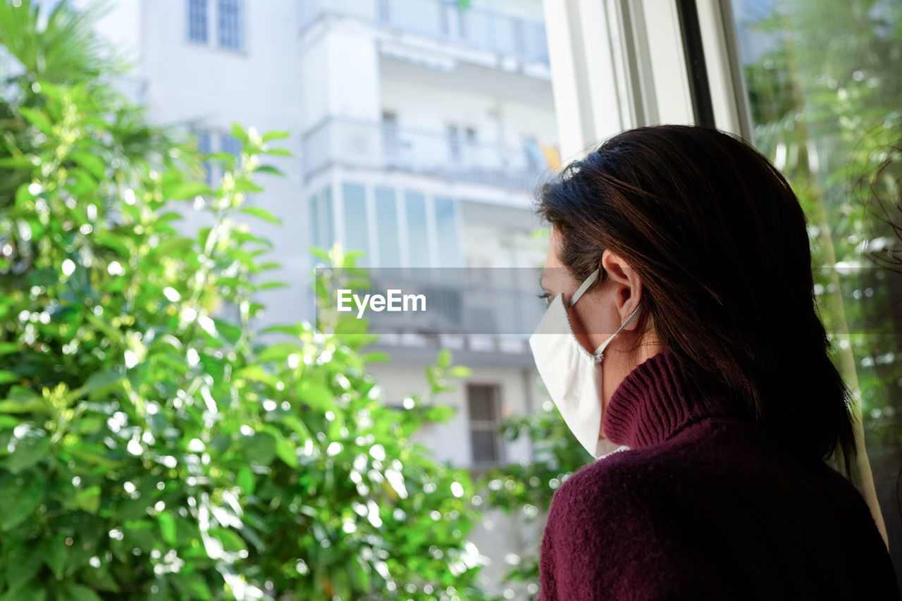 Woman wearing mask while looking through window