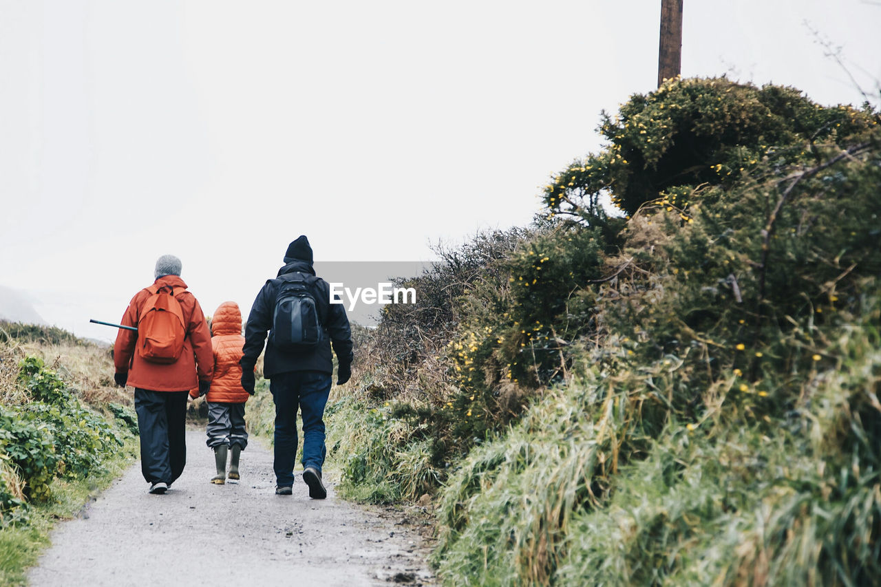 REAR VIEW OF PEOPLE WALKING ON ROAD