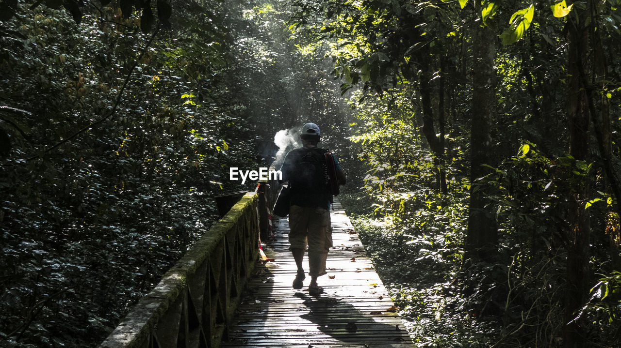 REAR VIEW OF MAN WALKING ON FOOTPATH