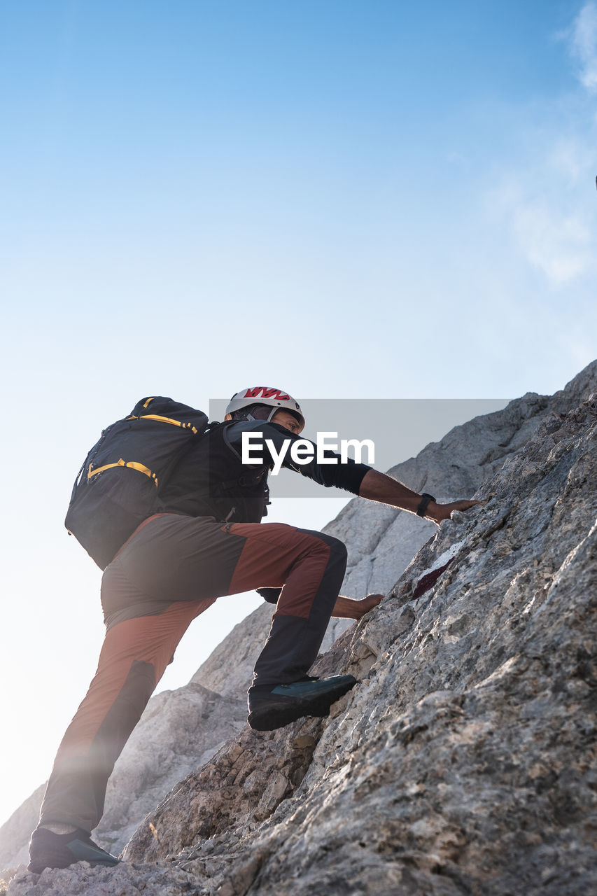 Mountaineer climbing on rocky wall under blue sky