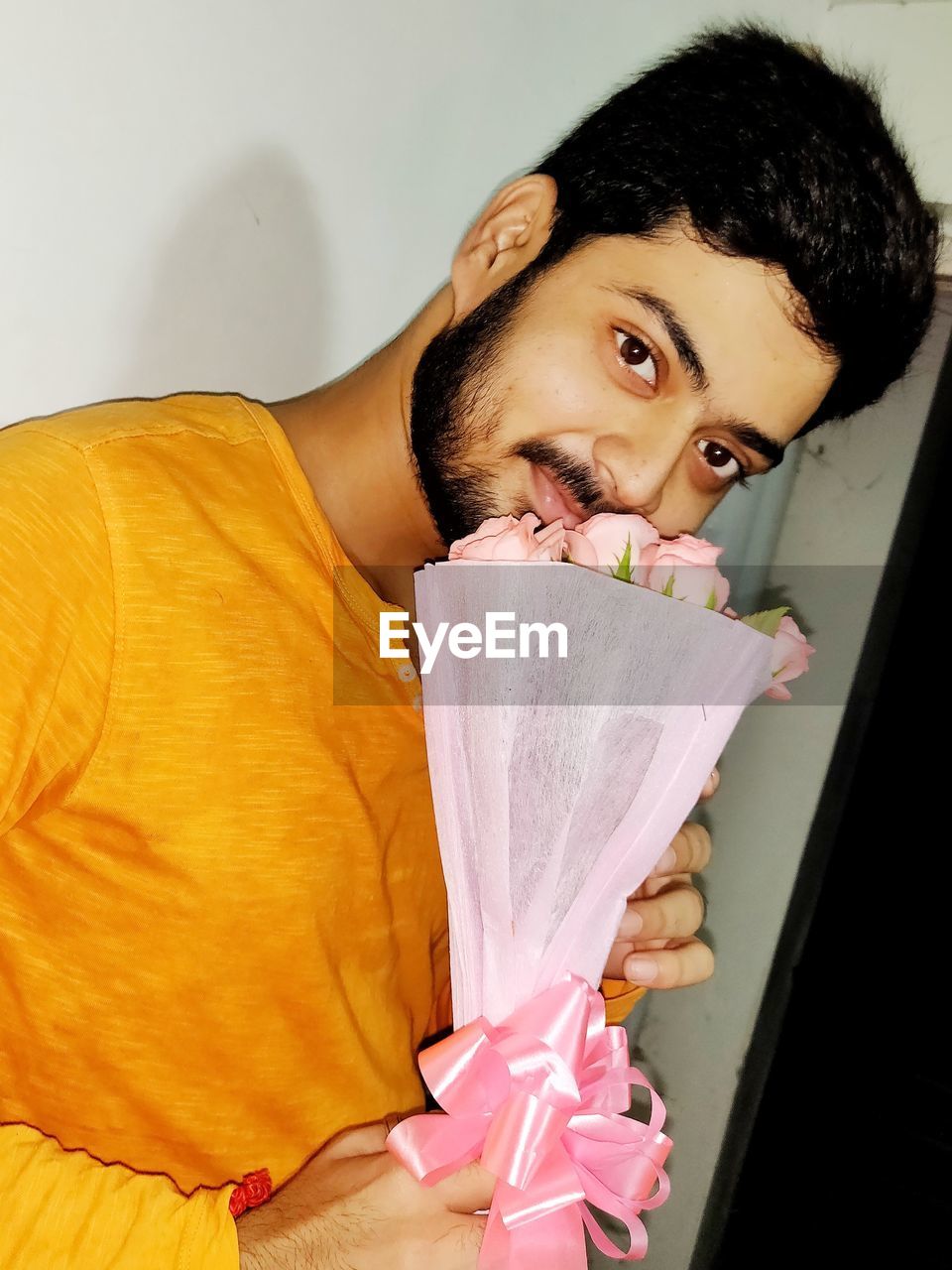 Portrait of young man holding rose flowers at home