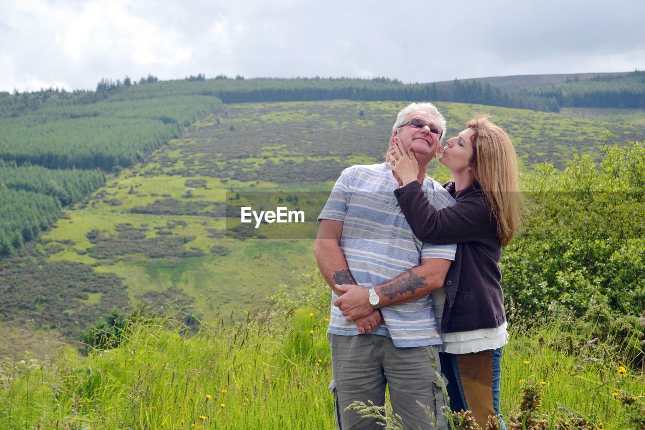 Mature woman kissing senior man while standing on field